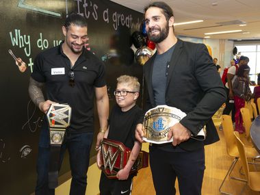 Le patient Jacob Mowl (patient, 15 ans) prend une photo portant l'une des ceintures des champions de la WWE avec Roman Reigns (polo noir) et Seth Rollins (veste). La WWE a amené certaines de leurs personnalités de lutte pour un événement énergique dans l'atrium des papillons du CHST Dallas où cinq patients ont eu la chance d'être costumés "Superstars" et être présenté à une foule enthousiaste.